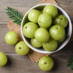 White bowl filled with Amla fruits on a wooden surface