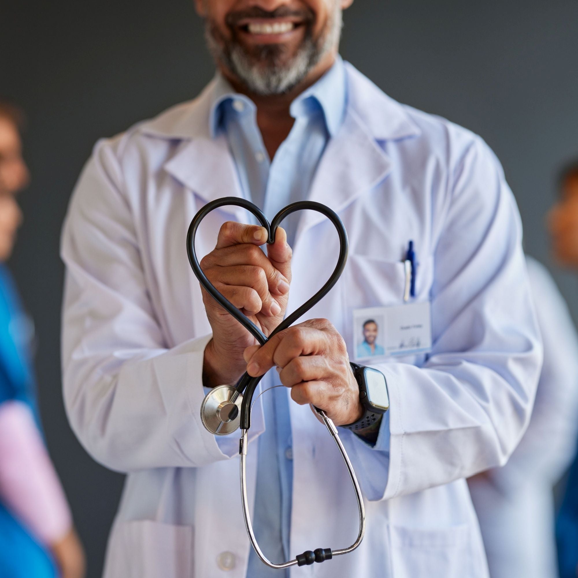 Doctor holding a stethoscope shaped like a heart with colleagues in the background