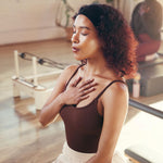 Woman in a Pilates studio with her eyes closed, holding her chest.