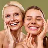 Two women touching their faces against a green background showing clear skin