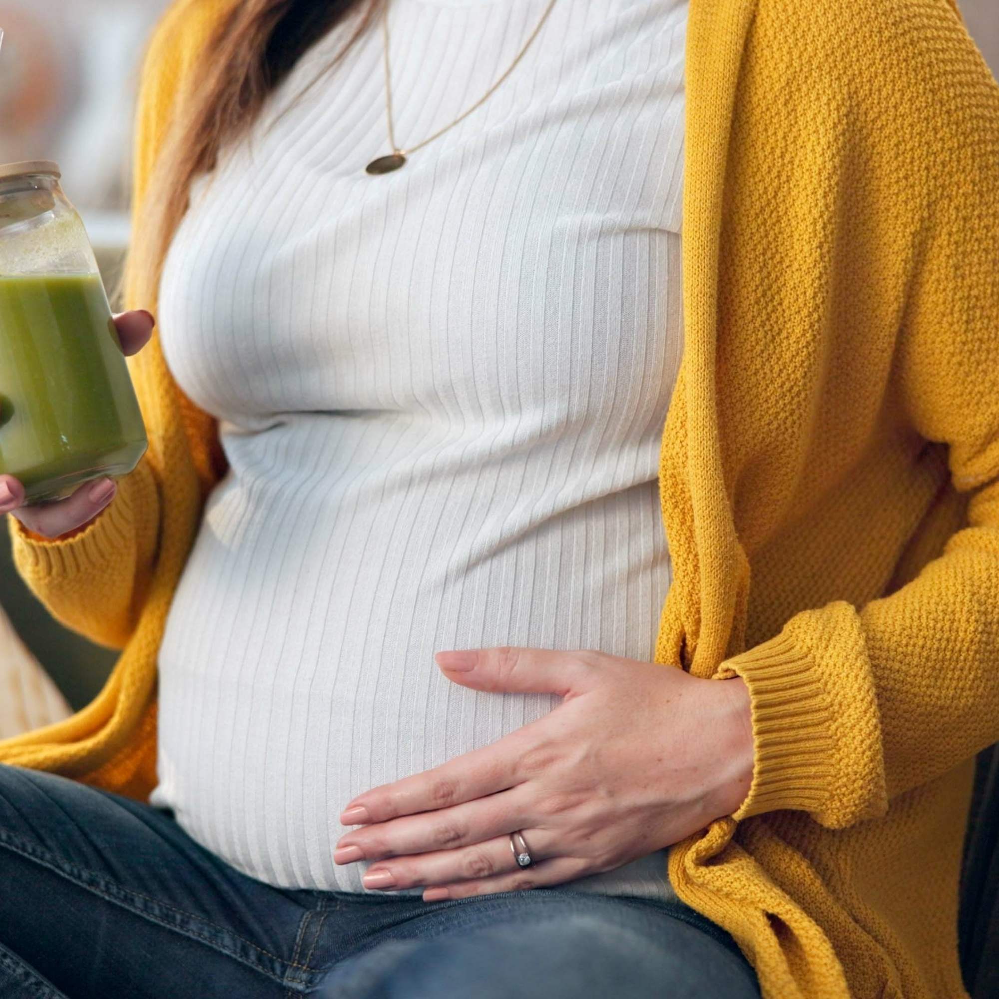 Pregnant person holding a glass of Bhringraj green juice and touching their belly.