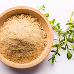 Wooden bowl filled with a brahmi powder next to green leaves on a white background