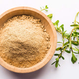 Wooden bowl filled with a brahmi powder next to green leaves on a white background