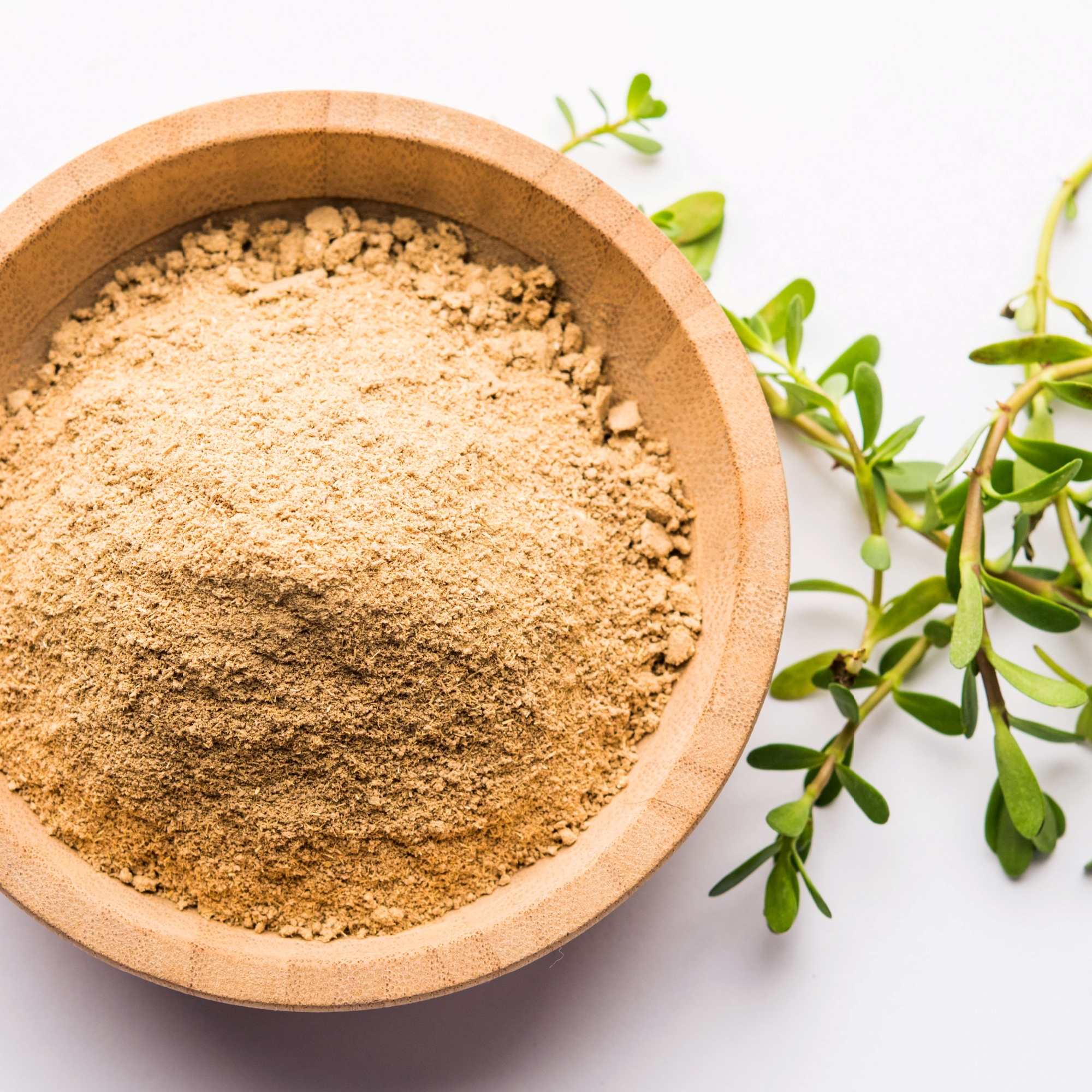 Wooden bowl filled with a brahmi powder next to green leaves on a white background