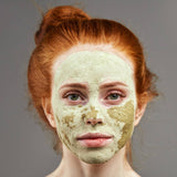 Woman with a centella facial mask on her face against a gray background