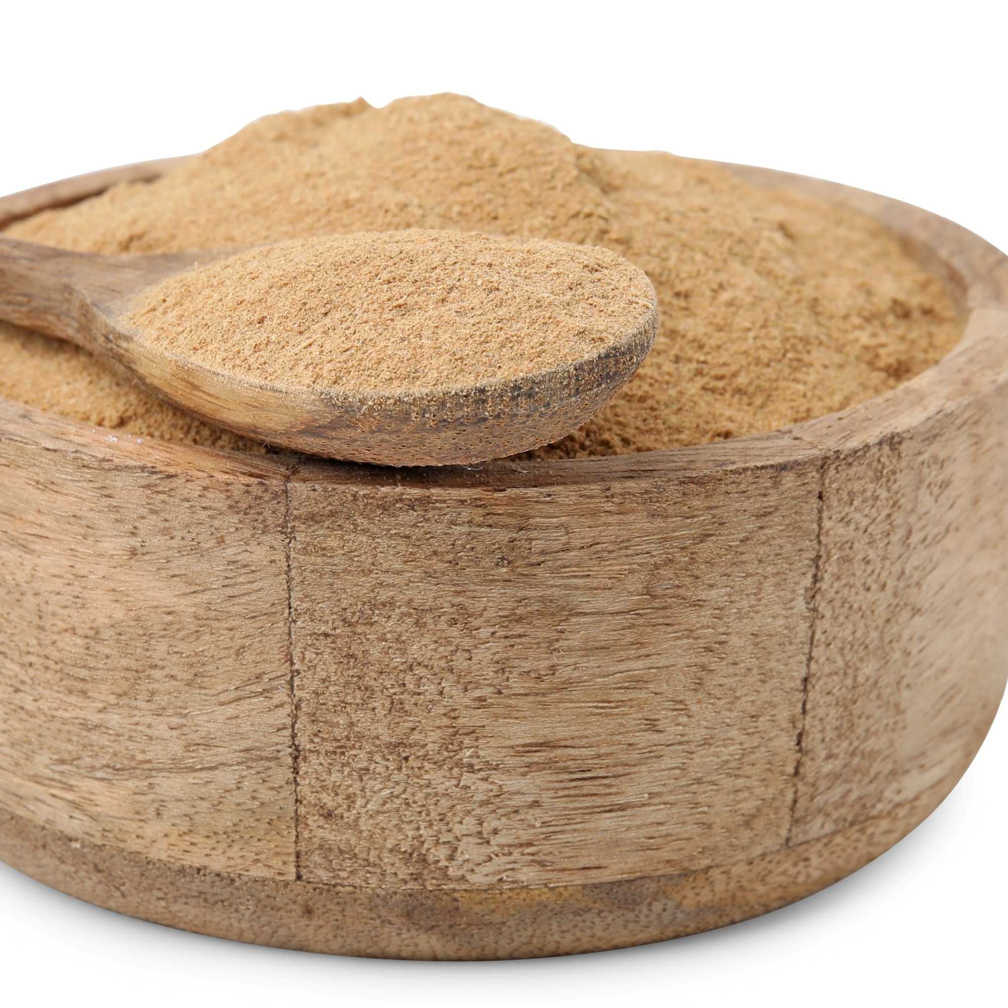 Wooden bowl filled with gokshura powder and a wooden spoon on a white background