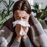 Person with a blanket and tissue, possibly ill or cold, with plants in the background