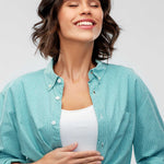 Woman wearing a teal button-up shirt over a white top on a light gray background