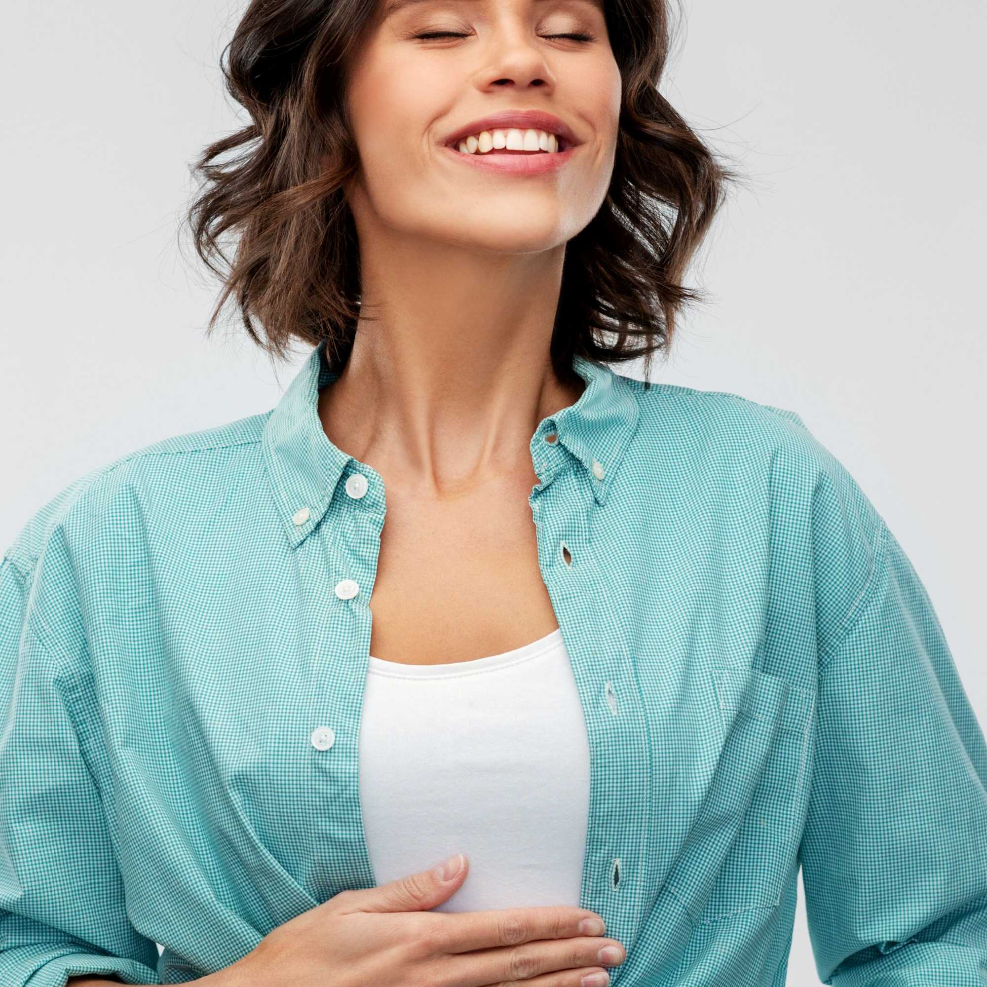 Woman wearing a teal button-up shirt over a white top on a light gray background