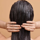 Person with wet hair covering their face against a beige background applying a herbal hair mask