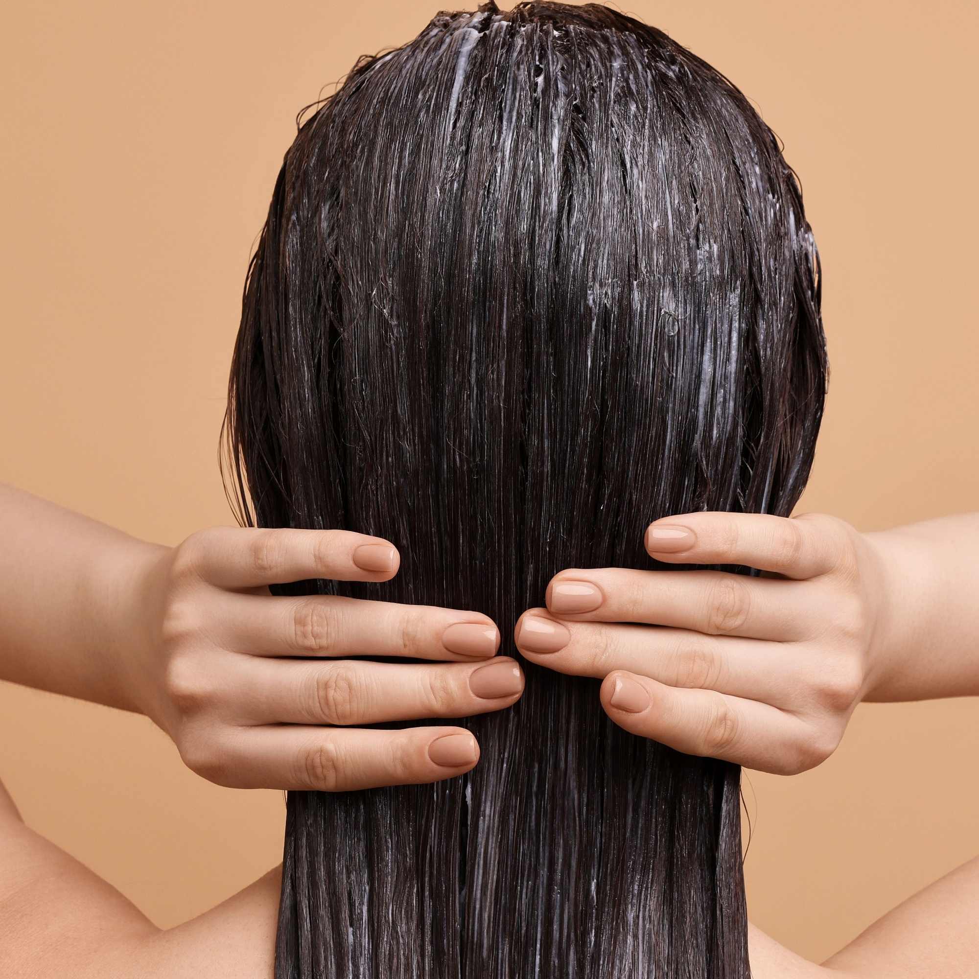 Person with wet hair covering their face against a beige background applying a herbal hair mask