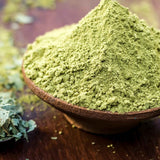 Ayumi Henna powder in a wooden bowl on a wooden surface with green leaves.