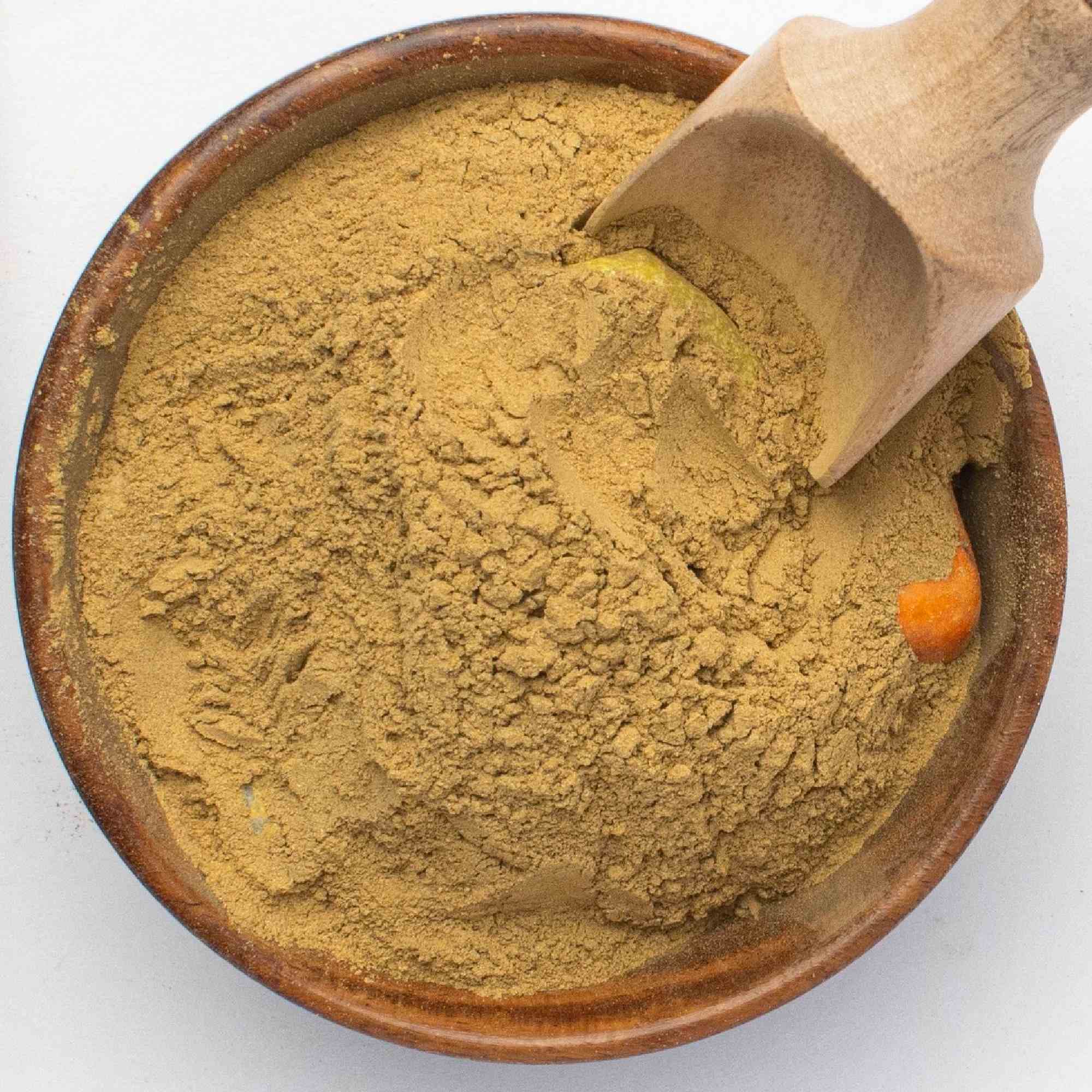 Wooden bowl filled with Himej powder and a wooden scoop on a white background