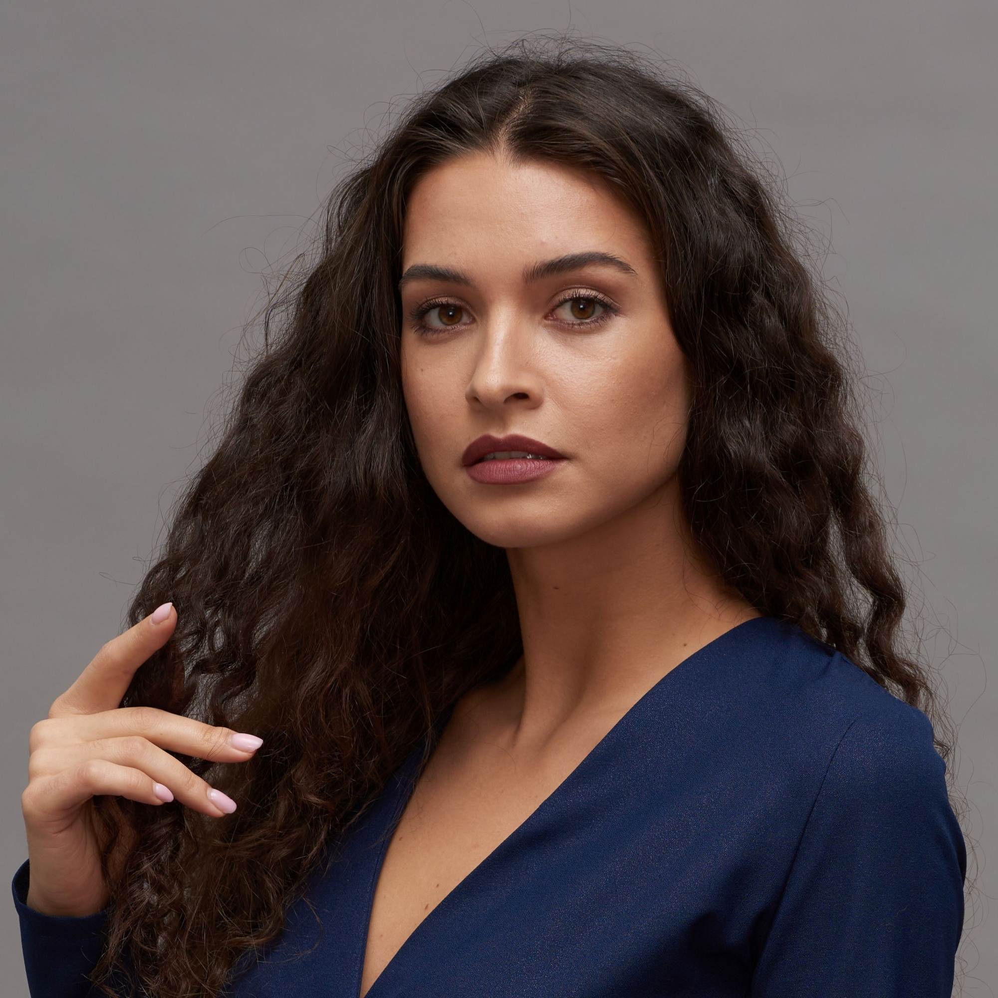 Woman with long, wavy hair wearing a blue top against a gray background