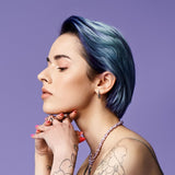 Person with blue hair and tattoos on a purple background
