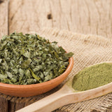 Moringa dried leaves in a clay bowl and Moringa Powder in a wooden spoon