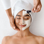 Woman receiving a facial mask treatment with a brush on a white background