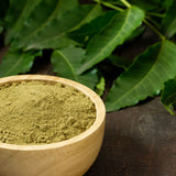 Neem LEAVES showing in the background and neem Powder showing in front in a wooden bowl