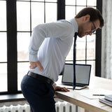 Man experiencing back pain feelings his kidneys at a desk with a laptop