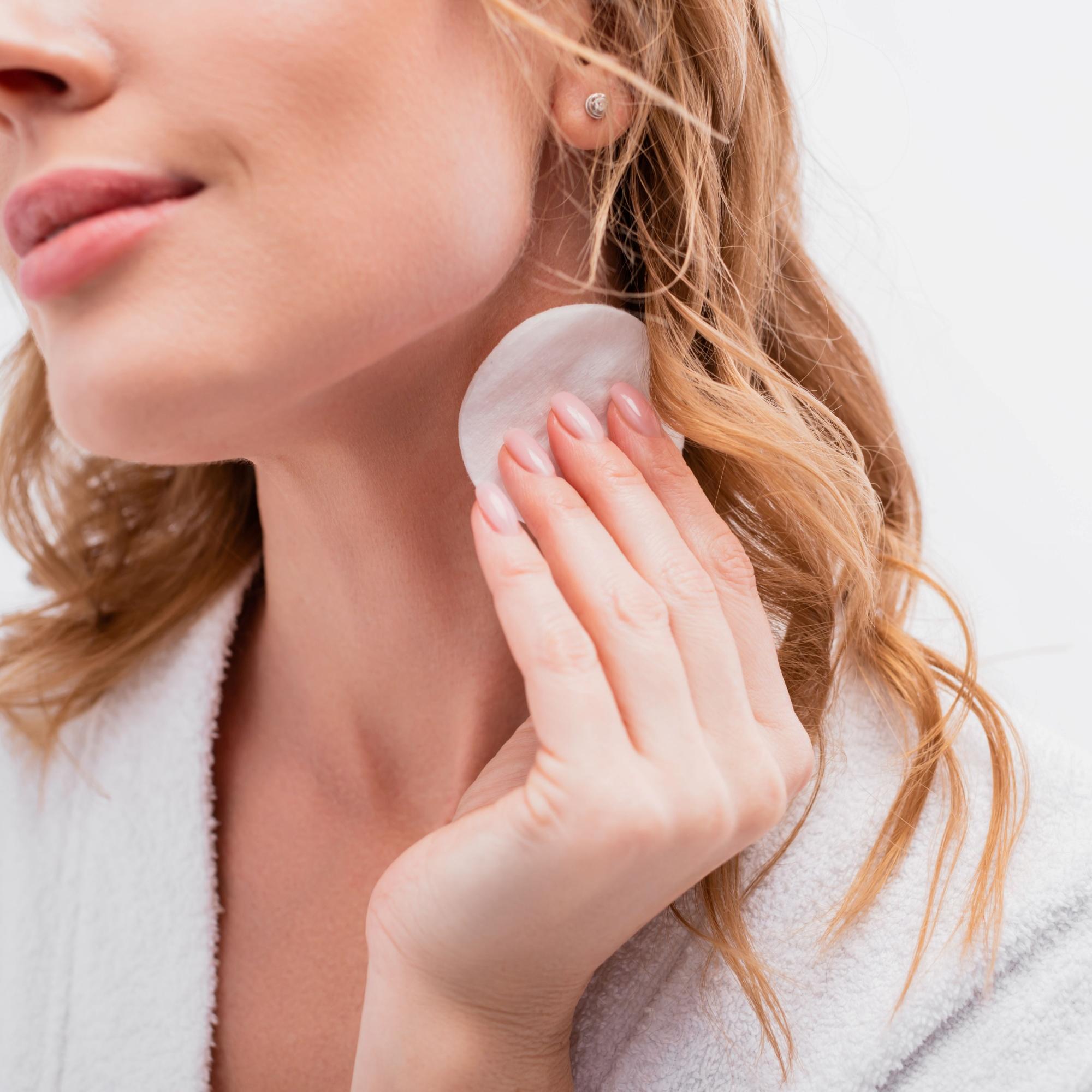Woman applying rose water to her face with a cotton pad.