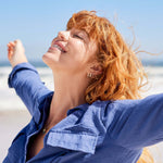 Woman with red hair and blue shirt laughing on a beach