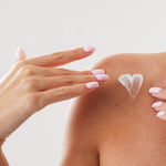 Hand applying Ayumi Sandalwood Body Lotion to shoulder with a heart shape on a light background