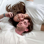 Two people lying on a bed, smiling and embracing.