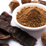 White bowl filled with brown powder surrounded by dried roots on a white background