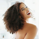 Woman with curly hair smiling against a bright background